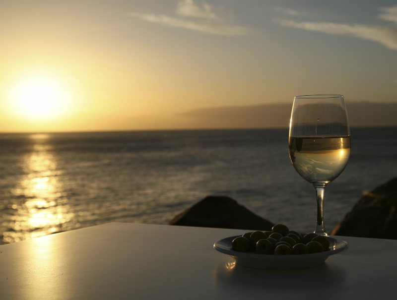 A glass of white wine over looking the sun setting over the sea.