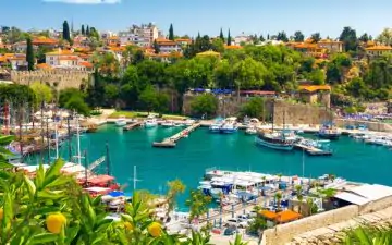 Side image of the Antalya old town harbour, with beautifully bright sea and lots of boats moored up in the harbour.