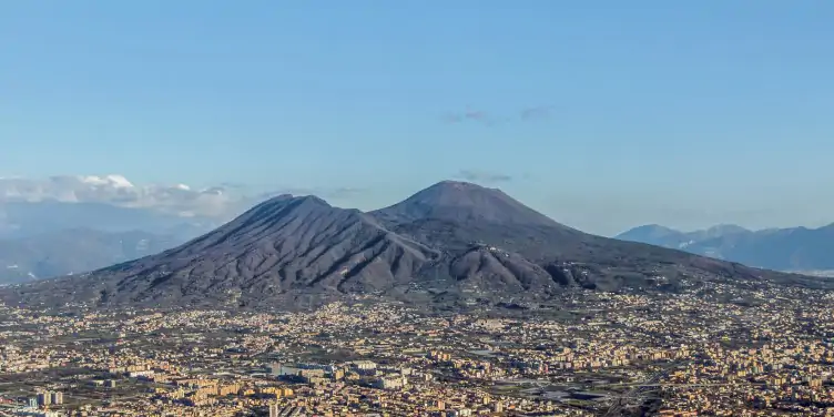 Landscape view of the Vesuvius famous volcano. With the neighbouring town just below it and a cloudy blue sky above it. 