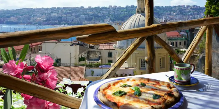 Close-up of a traditional Italian margarita pizza on a flowery balcony that overlooks the beautiful city of Naples.