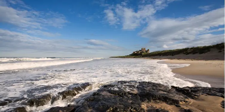 an image of the waves at Bamburgh Beach, with Bamburgh Castle in the distance