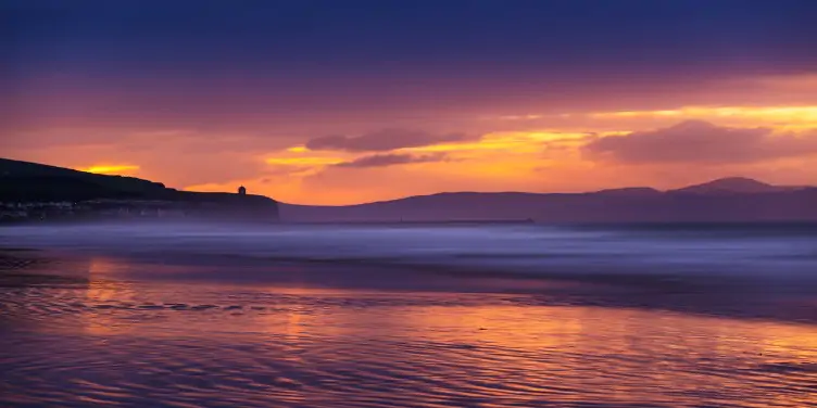 an image of the water at Portstewart Strand at sunset with the temple in the distance