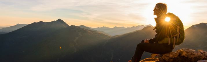 Woman sitting on a mountain peak at sunset