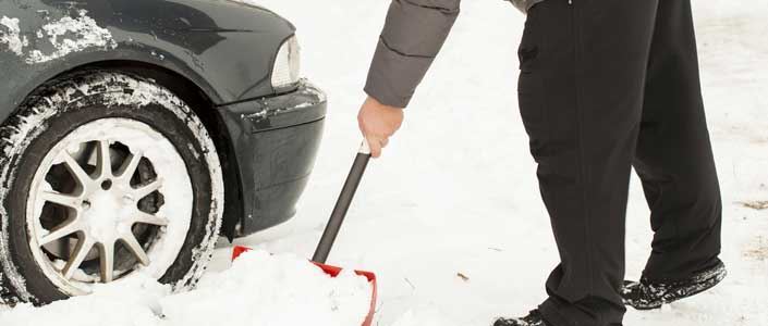 Man using shovel to dig car out of snow