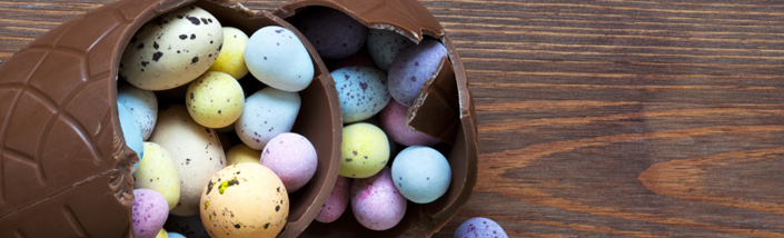 A Large chocolate easter egg spilling out smaller mini easter eggs in pastel colours
