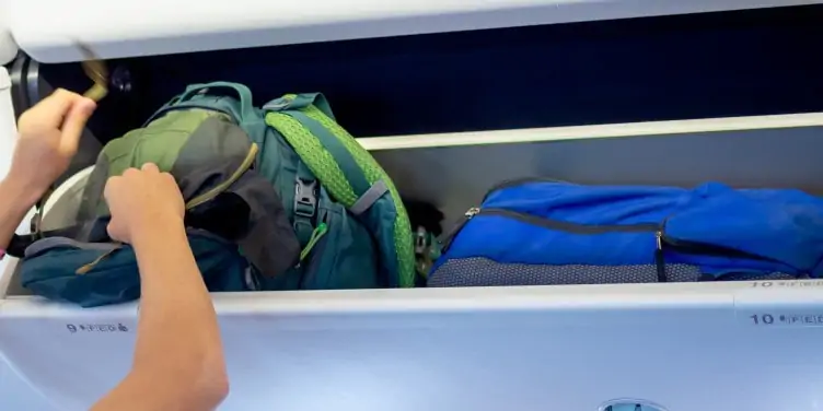 Person putting their luggage in the overhead lockers. 