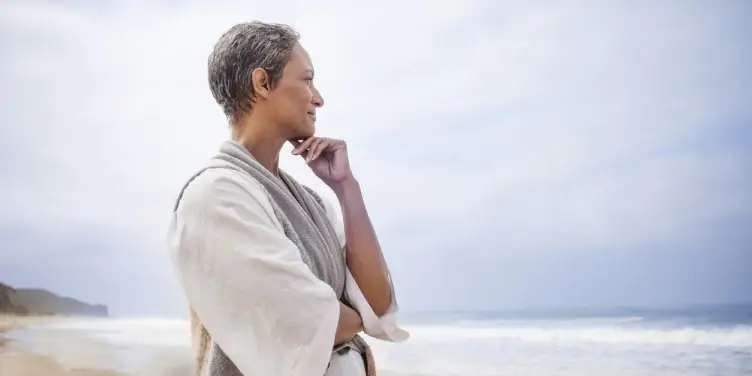 Mature women standing on a beach looking into the distance.