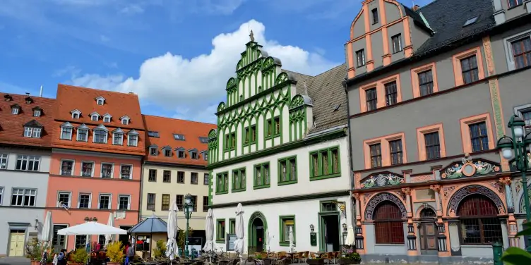 A view of old different shaped buildings from a courtyard in Weimar. Sitting outside are locals and tourists enjoying food and drinks. 