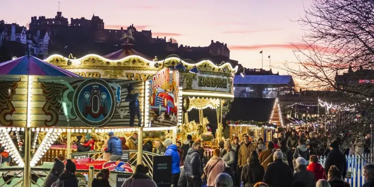 Edinburgh Christmas market lit up at dusk with Edinburgh Castle in the background