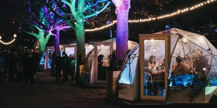 Row of Jimmy's Winter Lodge igloos on the southbank of River Thames at night with people inside drinking hot drinks.