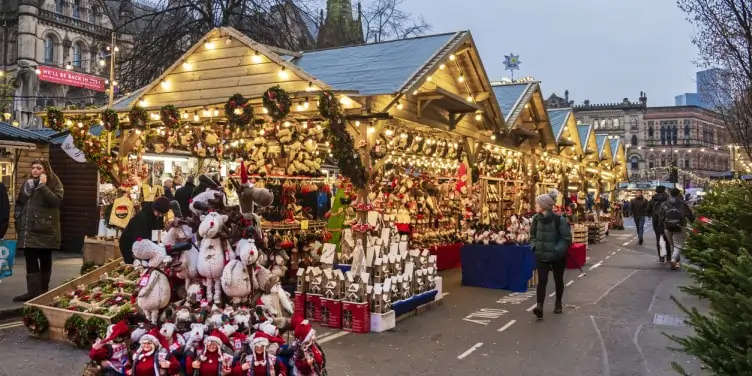 People walking along the Christmas market stalls lit up in Manchester