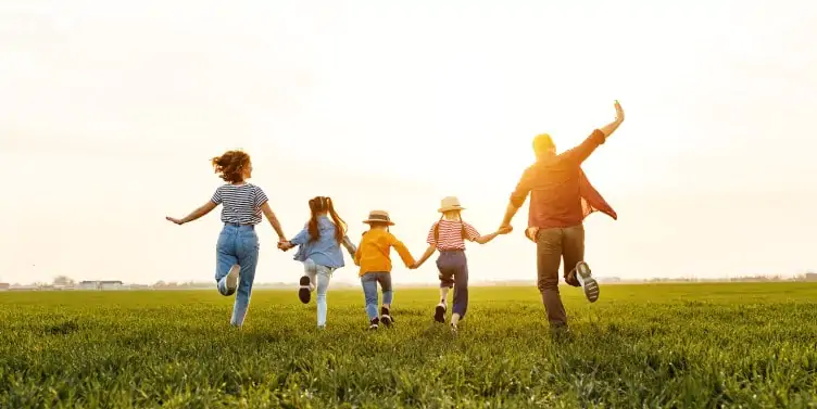 Family holding hands running on a field in summer
