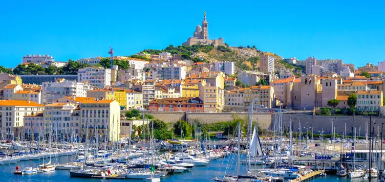 Beautiful French houses of Marseilles, gathered along the sea-front of a harbour filled with moored colourful boats.