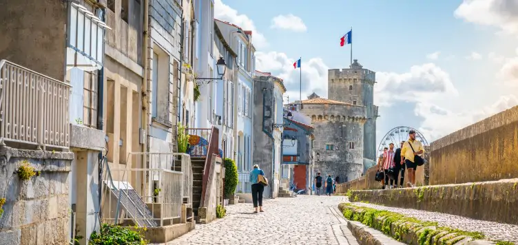 Blissful view of the Chain and Saint Nicholas Towers and Sur Les Murs Medieval cobbled streets with tourists walking in La Rochelle.