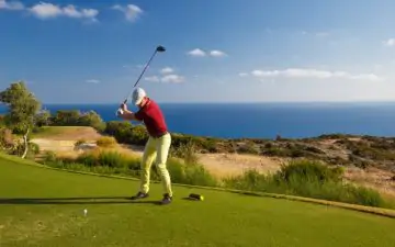 Male golfer teeing off against a background of the ocean