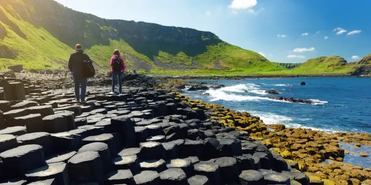 Two tourists walking at Giants Causeway, an area of hexagonal basalt stones, created by ancient volcanic fissure eruption.
