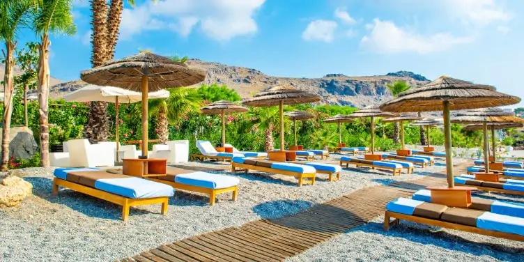Rocky beach with sunbeds and straw umbrellas on Rhodes island, Greece