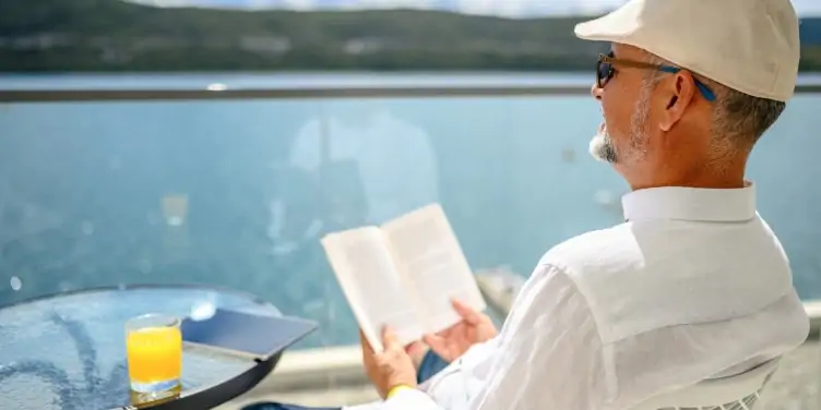 Man relaxes on a cruise ship balcony with a book and drink