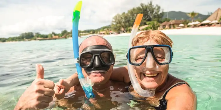 Senior couple giving the thumbs up while swimming in the sea with goggles and snorkels