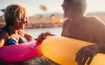 Older couple on holiday having fun in the sea with colourful inflatable rings