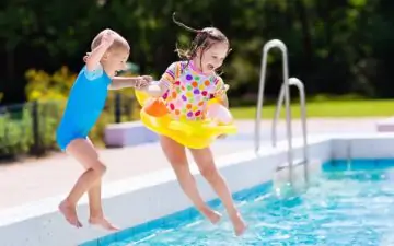 Kids holding hands jumping into outdoor swimming pool during family summer holiday