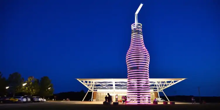 A neon, 66-foot-tall soda bottle stands in front of POPS 66 Soda Ranch against the nighttime sky.