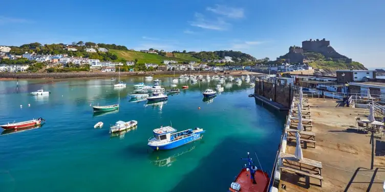 Stunning seaside town with a dock in Jersey, with moored fishermans boats and homes in the distance. 