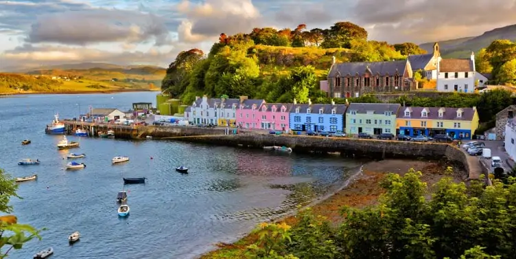 Pastel coloured houses looking out onto a small harbour and beach surrounded by countryside on the Isle of Skye, Scotland. 