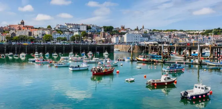 Beautiful harbour in Guernsey filled with fishing boats overlooked by buildings and houses. 