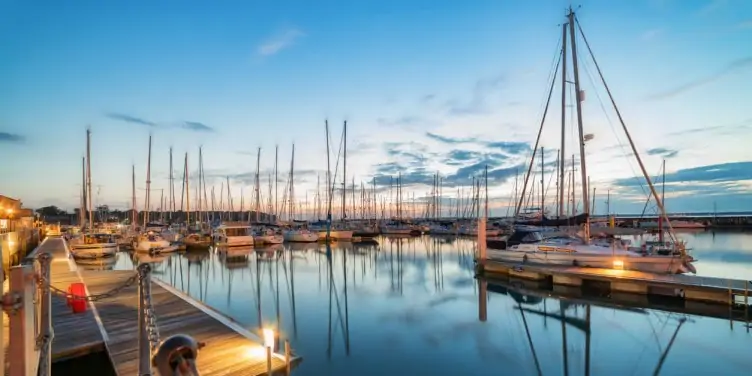 Attractive harbour on the Isle of Wight filled with boats on mirrored water from the setting sun. 