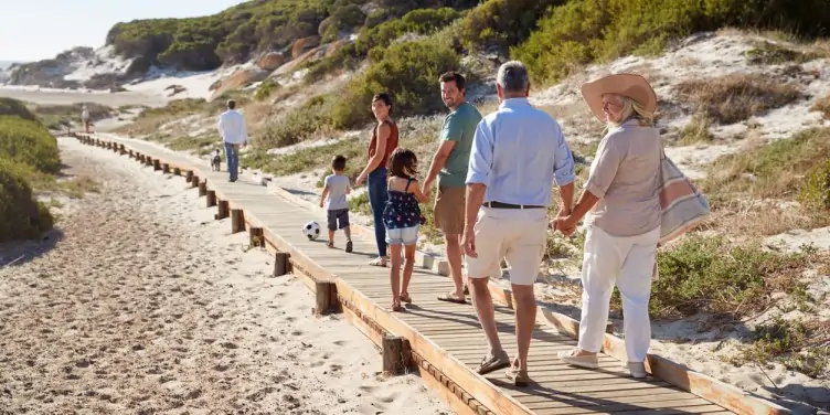 Three generation family walking along wooden promenade on beach