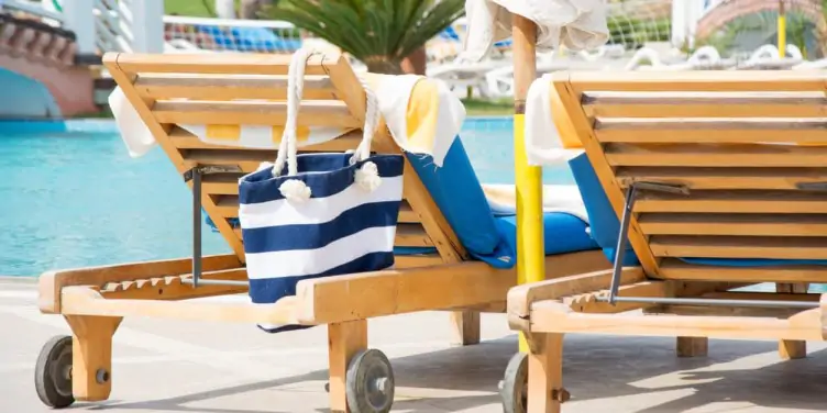 Two sun loungers beside the pool reserved with towels and a blue and white striped bag