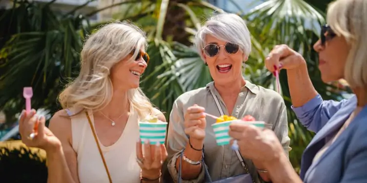 Senior female friends eating ice cream and shopping together in the city in summer