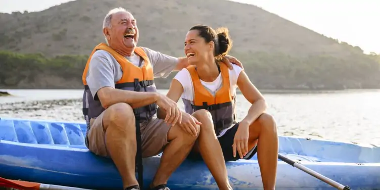 Senior male sitting on side of kayak with female overlooking a lake