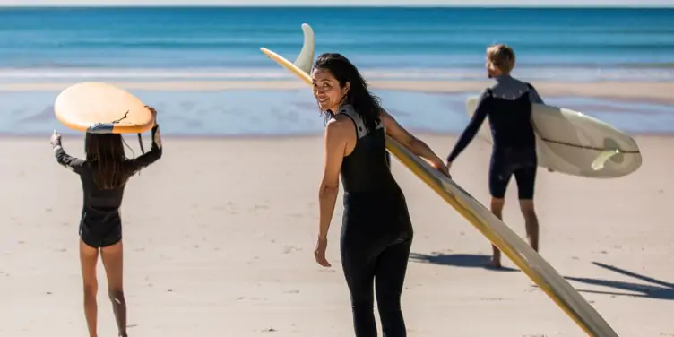 An older woman follows younger family members into the sea with a surfboard