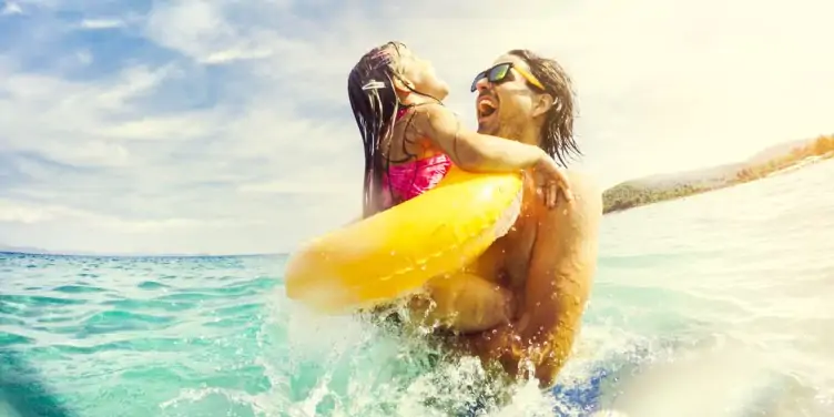 A father embraces his young daughter while having fun in the sea on holiday