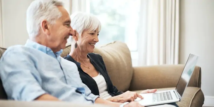  senior couple using their laptop while sitting on the sofa at home