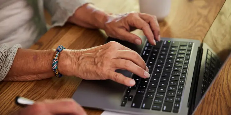 senior womans hands typing on laptop