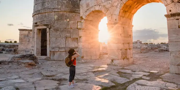 Female photographer tourist taking photos of ancient ruins in Greece at sunset