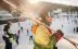 Skier wearing a helmet carries skis over her shoulder as she makes her way through a crowd of people at a popular skiing resort in Europe.