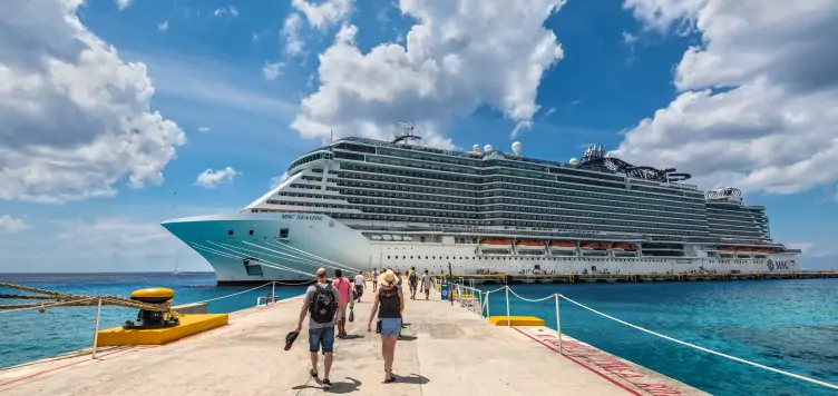 Group of people walking aboard a large cruise ship, ready to set sail. 