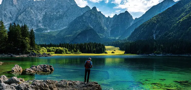 Elderly man standing on a rock surrounded by beautiful blue sea and mountains in the distance. 