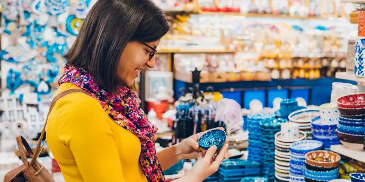 Tourist browsing a shop on holiday and picking up a trinket dish, surrounded by beautiful ceramic souvenirs and gifts. 