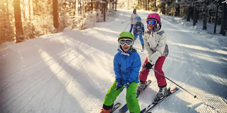 A young family of 4 in bright ski wear enjoying a ski run through a snowy national park.