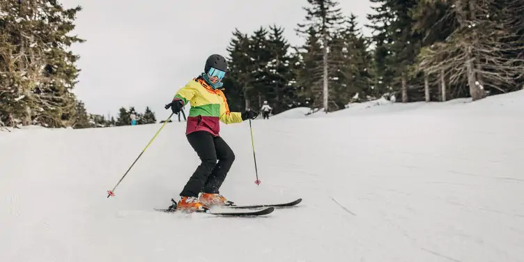 Skier in a multi-coloured jacket makes her way down the slope at speed, with a few other skiers in the distance at a unique ski resort in Europe.
