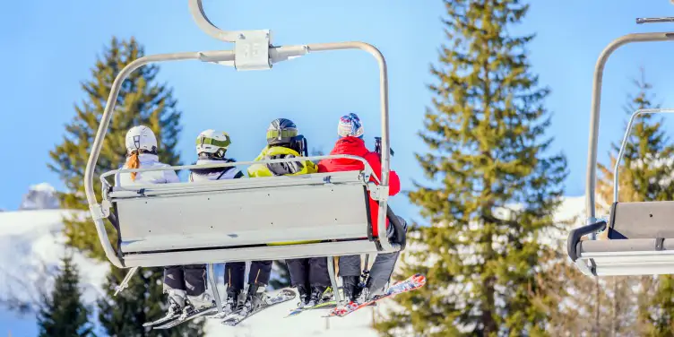 Ski lift carrying skiers in colour ski jackets and trousers up to the top of their favourite ski run. 