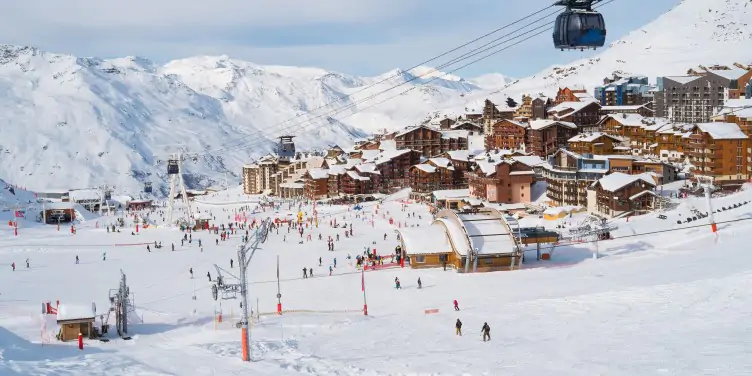 Snow covered village sits in the valley between mountains near a popular ski area.