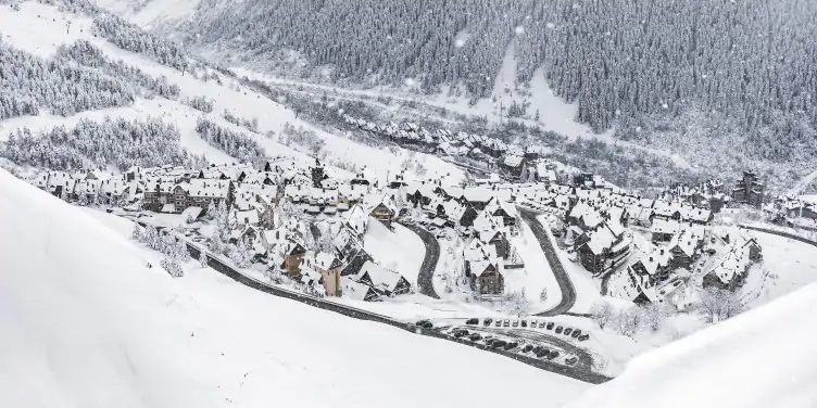 Wide shot of a busy ski resort in Europe, with skiers and accommodation in the distance against the background of the mountains.