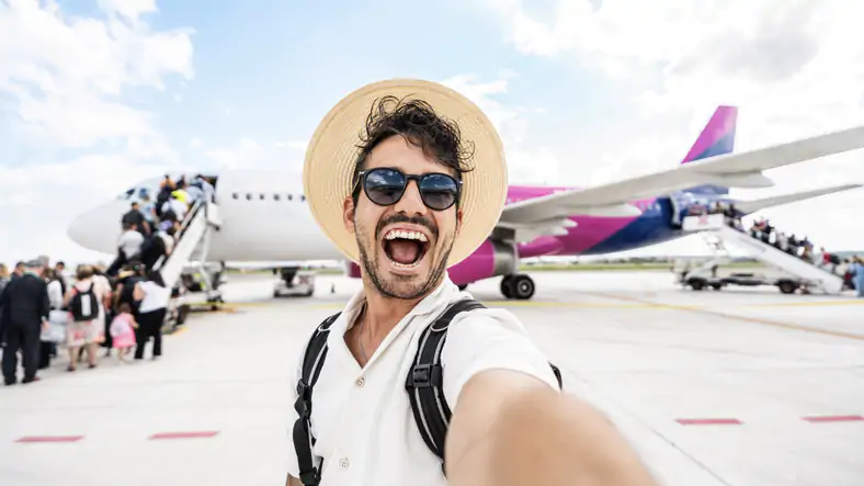 Happy tourist boarding on a plane at the airport - Handsome young man taking selfie picture in front of airplane - Summertime holidays and transportation life style concept